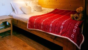 Une chambre dans une cabane en bois, avec un lit superposé, une couverture rouge et un ours en peluche.
