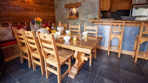 Une table de salle à manger en bois avec des chaises, un mur en pierre, des armoires en bois et un réfrigérateur.