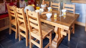Une table à manger en bois avec des chaises, un mur en pierre et un coin cuisine.