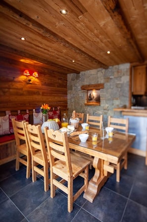 Une table Ă manger en bois avec des chaises, un mur en pierre et un coin cuisine.