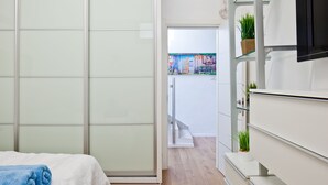 Ett modernt hotellrum med en skjutdörr i glas som leder ut till en balkong, en säng med ett blått handduk och en vit byrå med en platt-TV.