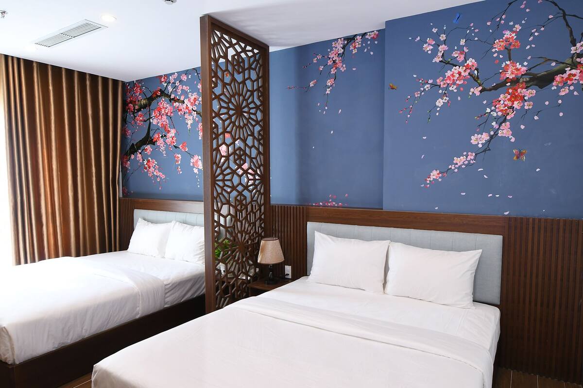 Een hotelkamer met twee bedden, een decoratieve wand met kersenbloesem afbeeldingen, en een houten scheidingswand.