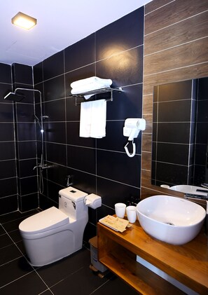 A modern bathroom with a black tiled wall, a white toilet, a large sink, and a handheld hair dryer mounted on the wall.