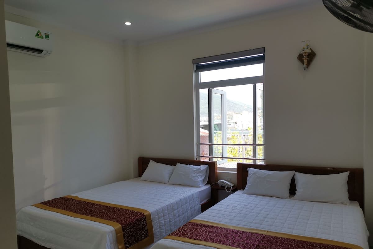 Une chambre d’hôtel avec deux lits simples, une grande fenêtre, un appareil de climatisation et un luminaire fixé au mur.