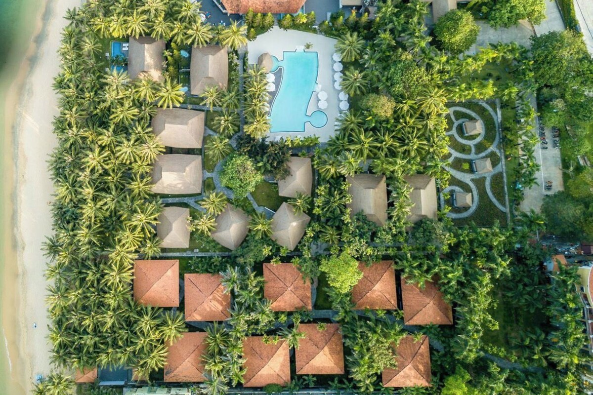 An aerial view of a resort with a swimming pool, multiple bungalow-style accommodations, and a beach.