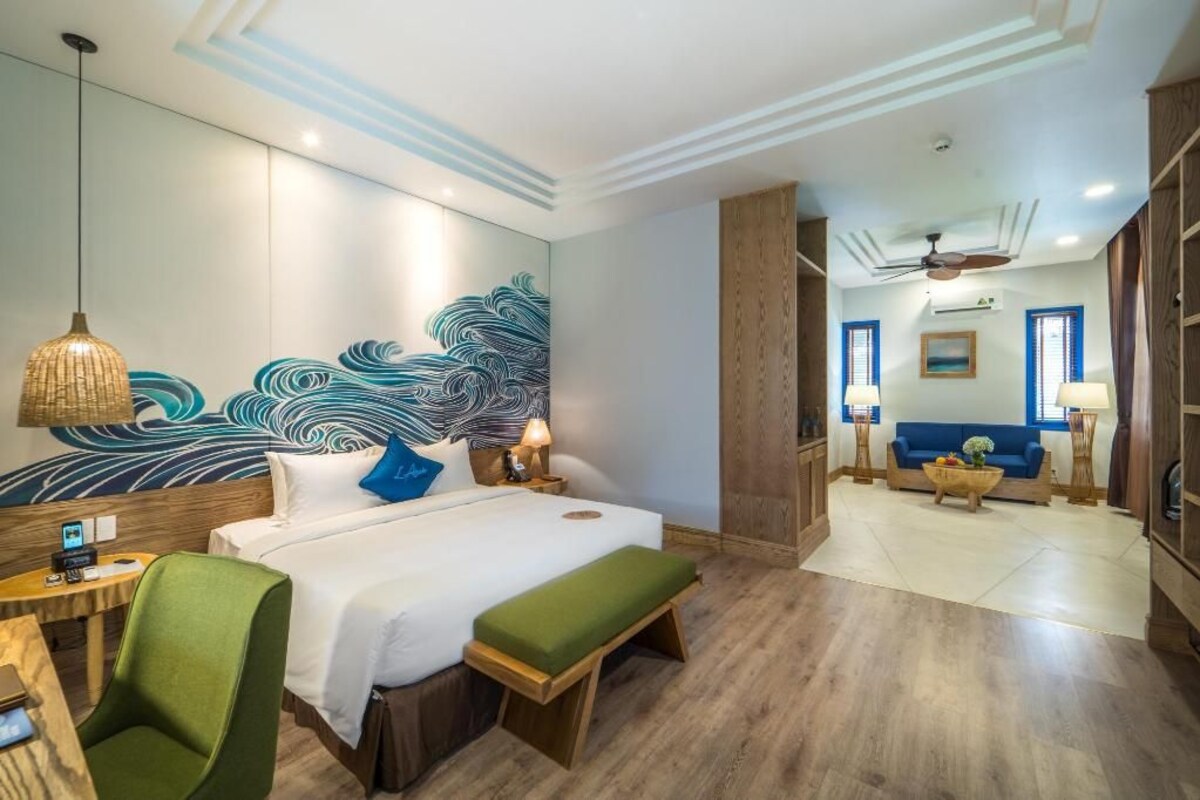 A hotel room with a bed, green chair, bedside table, and a wall with a wave pattern.