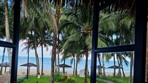 A view from inside a room looking out to a beach with palm trees and umbrellas. - L'Azure Resort and Spa (Phu Quoc)