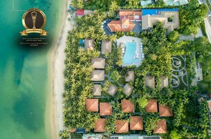 Vista aérea de un resort de lujo con villas frente a la playa, una piscina y exuberante vegetación.