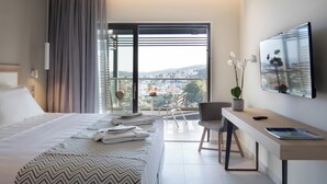 Una moderna camera d'albergo con un grande letto, una scrivania, una sedia, una televisione e un balcone con vista sulla città.