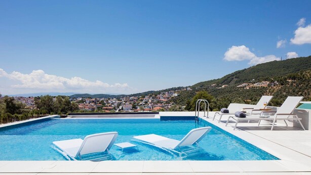 Una piscina con poltrona a sdraio bianche e vista su una cittadina collinare.