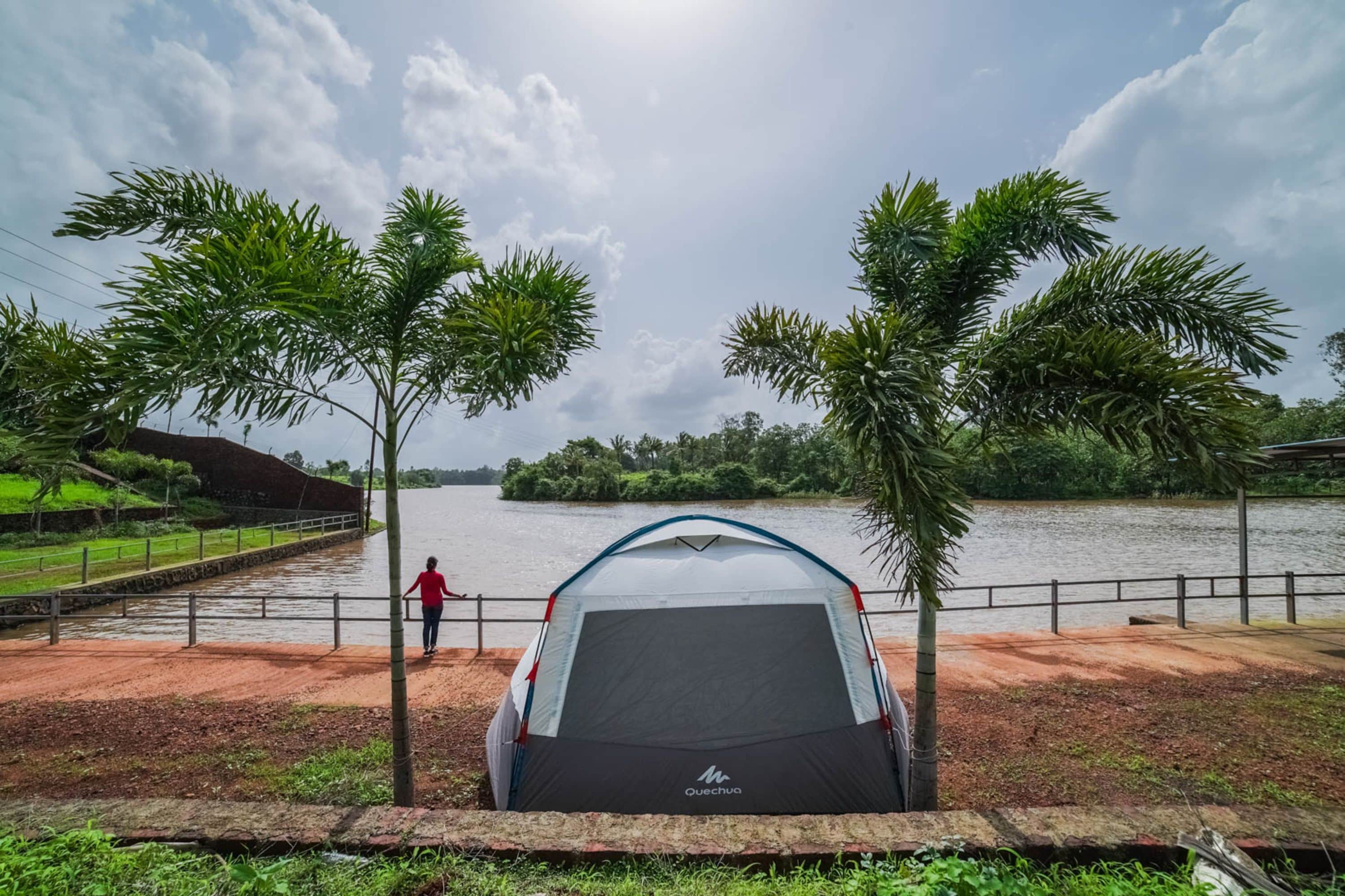 A tent with a black base and a white top, surrounded by palm trees and a body of water.