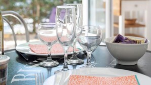Una mesa de comedor con cristalería transparente y platos, un bol con verduras moradas, y vistas a la vegetación a través de una ventana.