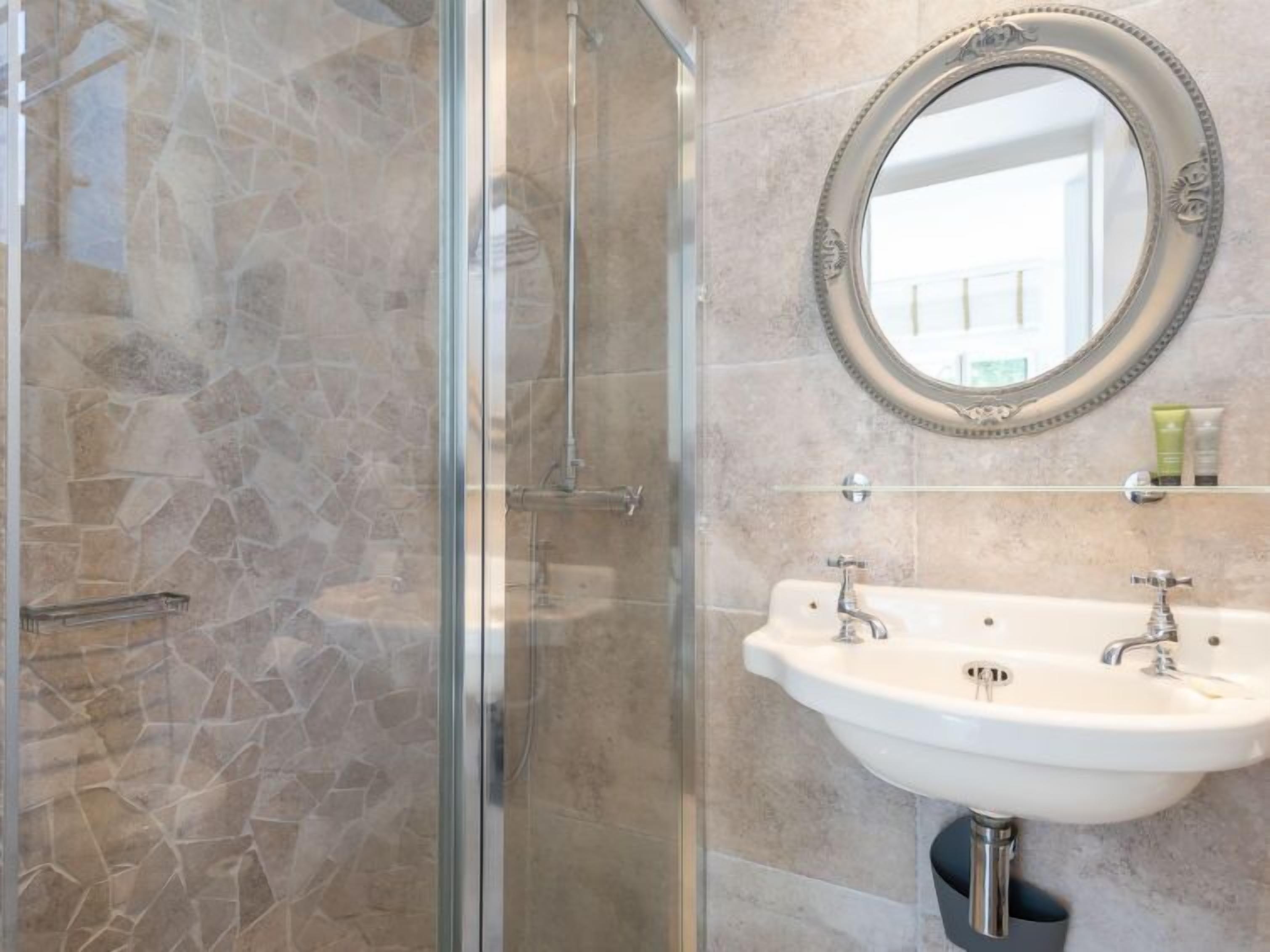 A bathroom with a glass-enclosed shower, a white sink, and a decorative mirror.
