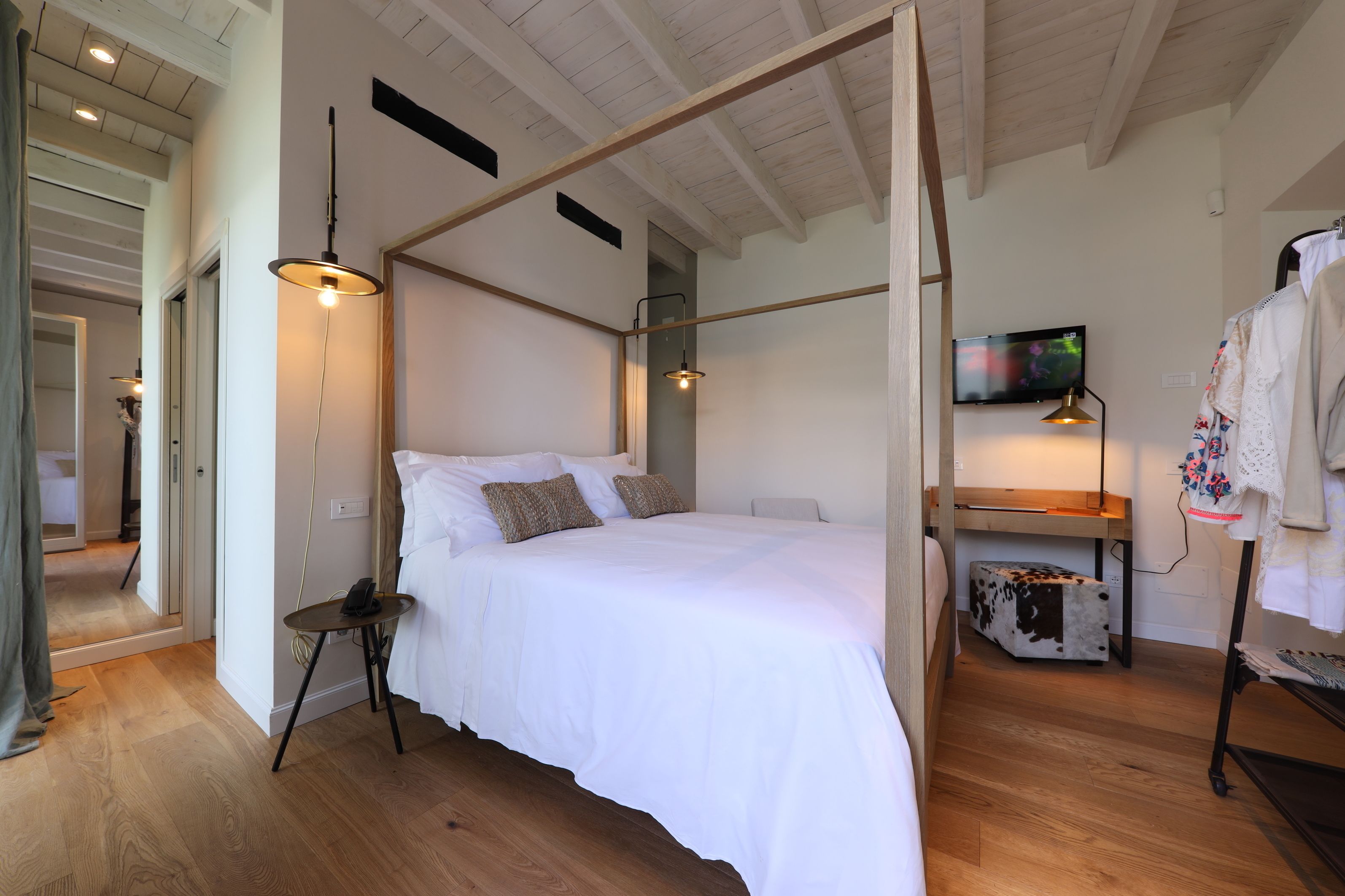 Una camera da letto moderna con un letto a baldacchino, una scrivania in legno, una televisione e un appendiabiti.