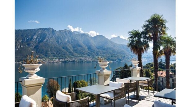An outdoor terrace with a view of a lake and mountains, featuring tables and chairs, and a decorative urn. - Villa Mojana, Limonta, Bellagio | The D’Angelo Family Collection (Oliveto Lario)