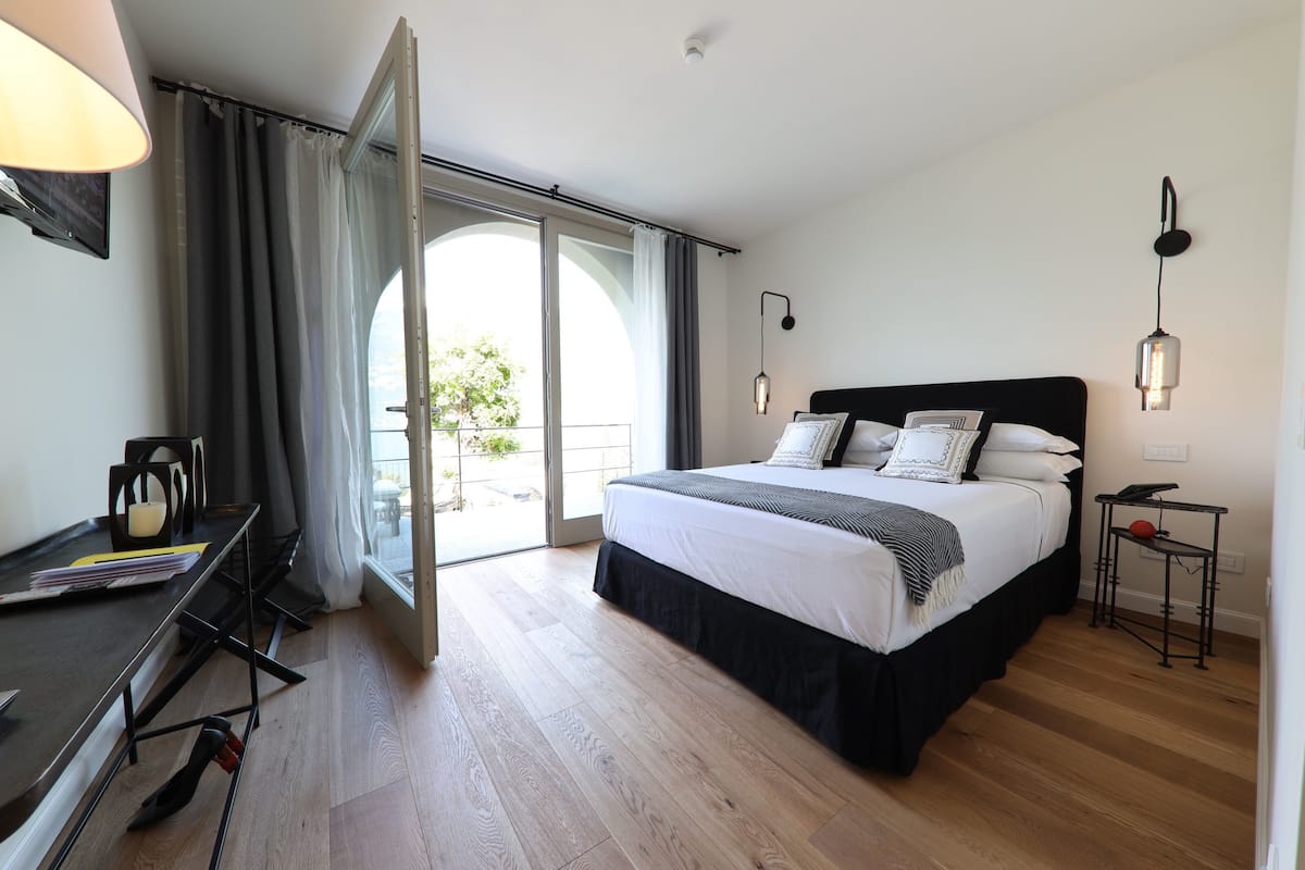 A modern bedroom with a large bed, a desk, and a balcony with curtains.