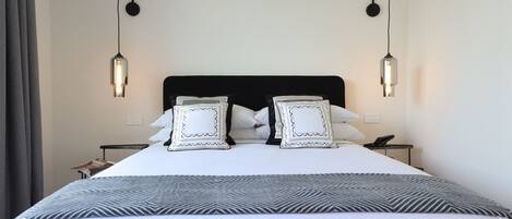 A neatly made bed with a black headboard, white bedding, and decorative pillows. There are two bedside tables with lamps and a small table with a telephone.
