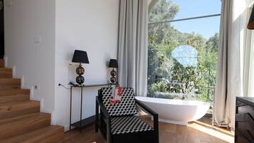 Un bagno moderno con una vasca freestanding, una sedia a scacchi bianchi e neri, e un'ampia finestra con vista su del verde.