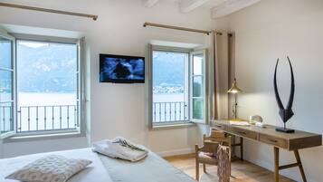 A bedroom with a bed, a desk, and a TV. There are windows with a view of mountains and a balcony.