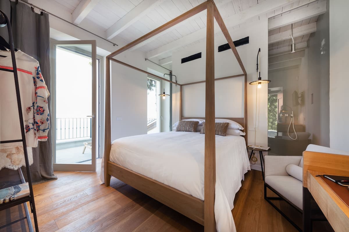 A bedroom with a four-poster bed, a desk, a chair, and a large window.
