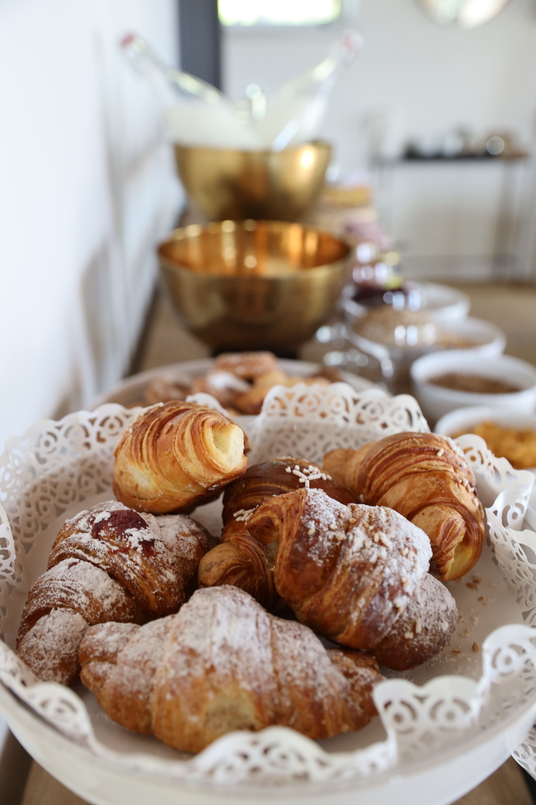 Uma bandeja com diversos doces, incluindo croissants e itens cobertos com açúcar em pó, sobre um jogo americano de renda.