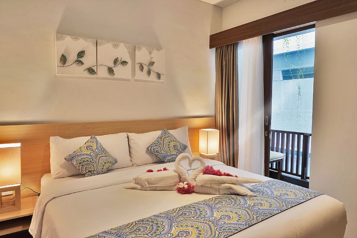 Ein Hotelzimmer mit einem großen Bett, zwei Nachttischlampen, einem Wanddekor und einem Balkon mit Blick.