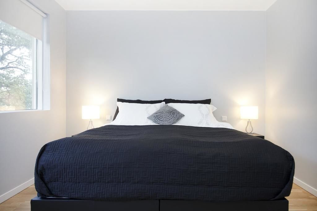 A bedroom with a large bed, two bedside lamps, and a window with a view of trees.