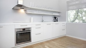 A modern kitchen with white cabinetry, a built-in oven, a coffee maker, and shelves with glasses and cups. - Blue Luxury Apartments (Reykjavik)