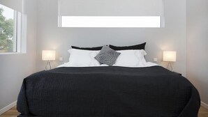 A modern bedroom with a large bed, two bedside lamps, and a window above the bed. - Blue Luxury Apartments (Reykjavik)