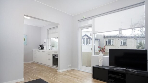 A modern living room with a large window, a flat-screen TV, and a black entertainment unit. - Blue Luxury Apartments (Reykjavik)