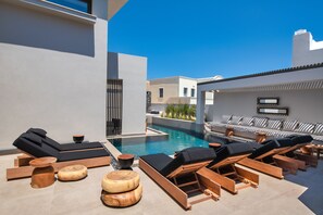 Un espace piscine extérieur moderne, doté de chaises longues et de tabourets en bois.