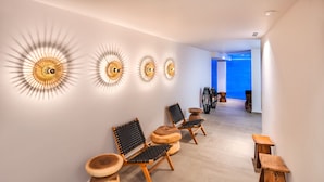 Un pasillo con sillas y mesas modernas, apliques decorativos en la pared y vista a otra habitación.