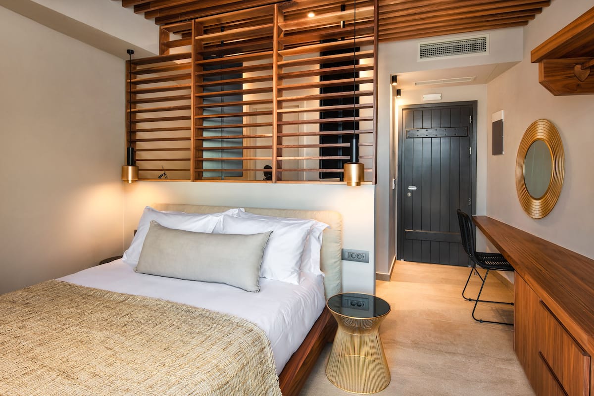 A bedroom with a bed, bedside table, lamp, and a wooden slatted headboard.