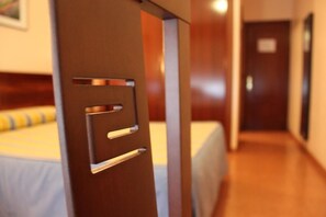 A hotel room with a bed, a wooden door with a handle, and a hallway leading to another room. - Hotel Valdés (Gijon)