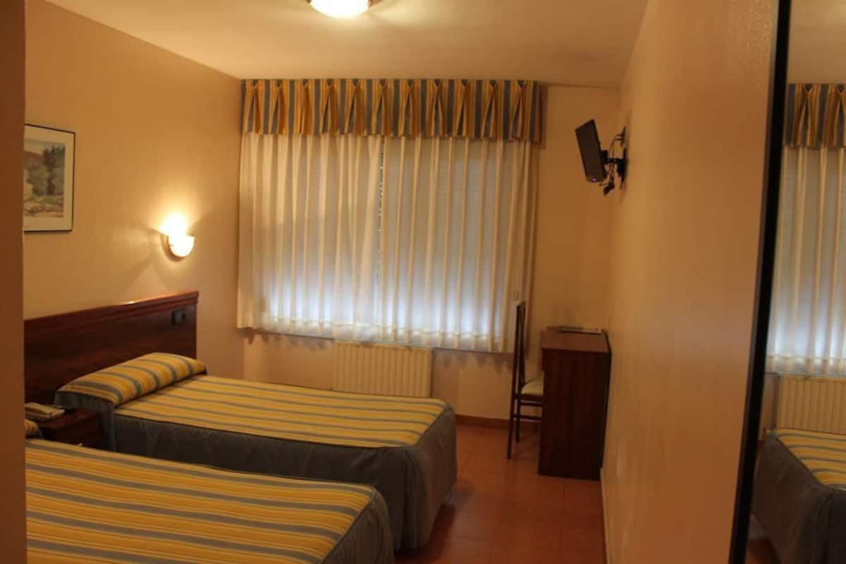 A hotel room with two beds, a desk, a chair, and a window with curtains.