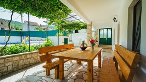 Una mesa de madera con bancos en un patio de piedra, un cuenco de fruta y un jarrón de flores.