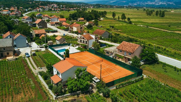 Vista aérea de una zona residencial con casas, una cancha de tenis y viñedos.