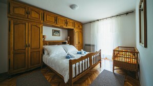 Un dormitorio con una cama de madera, un armario de madera, una cuna y un cuadro en la pared.