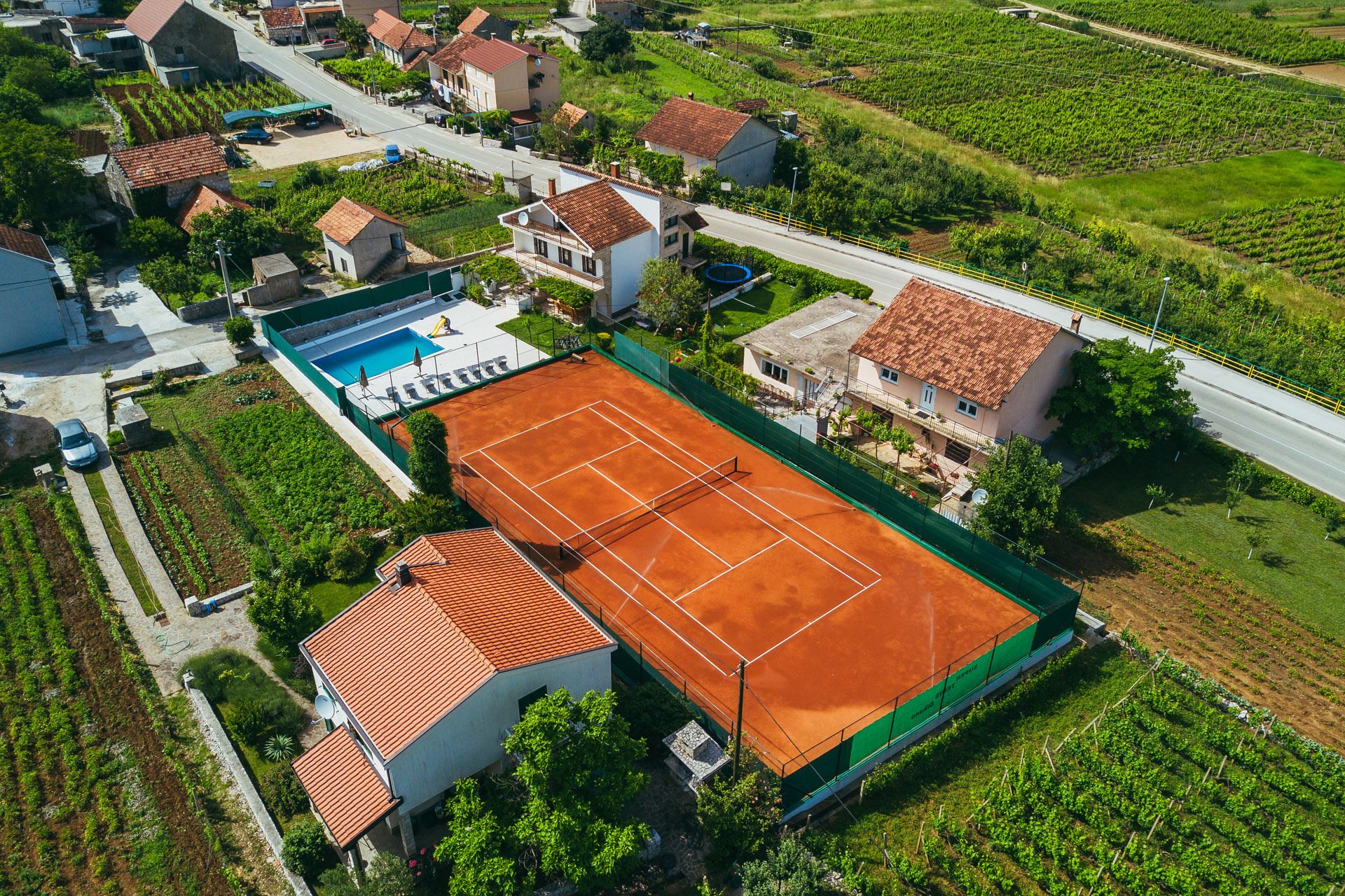 An aerial view of a residential area with houses, a tennis court, and vineyards.