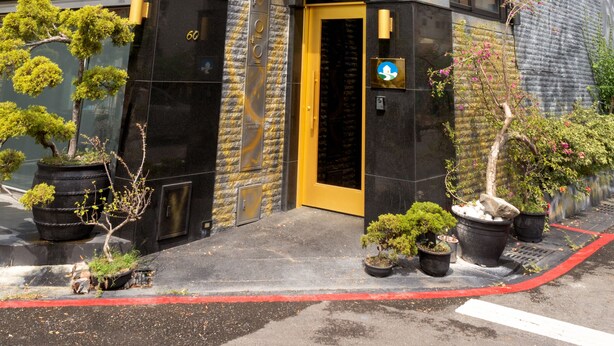Un edificio moderno con fachada negra y dorada, una puerta amarilla y plantas en macetas en el suelo.