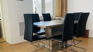 A dining area with a wooden table and four black chairs with chrome legs. There is a window with a view of buildings outside, and a radiator is visible on the wall. - City Pension Bremerhaven (Bremerhaven)