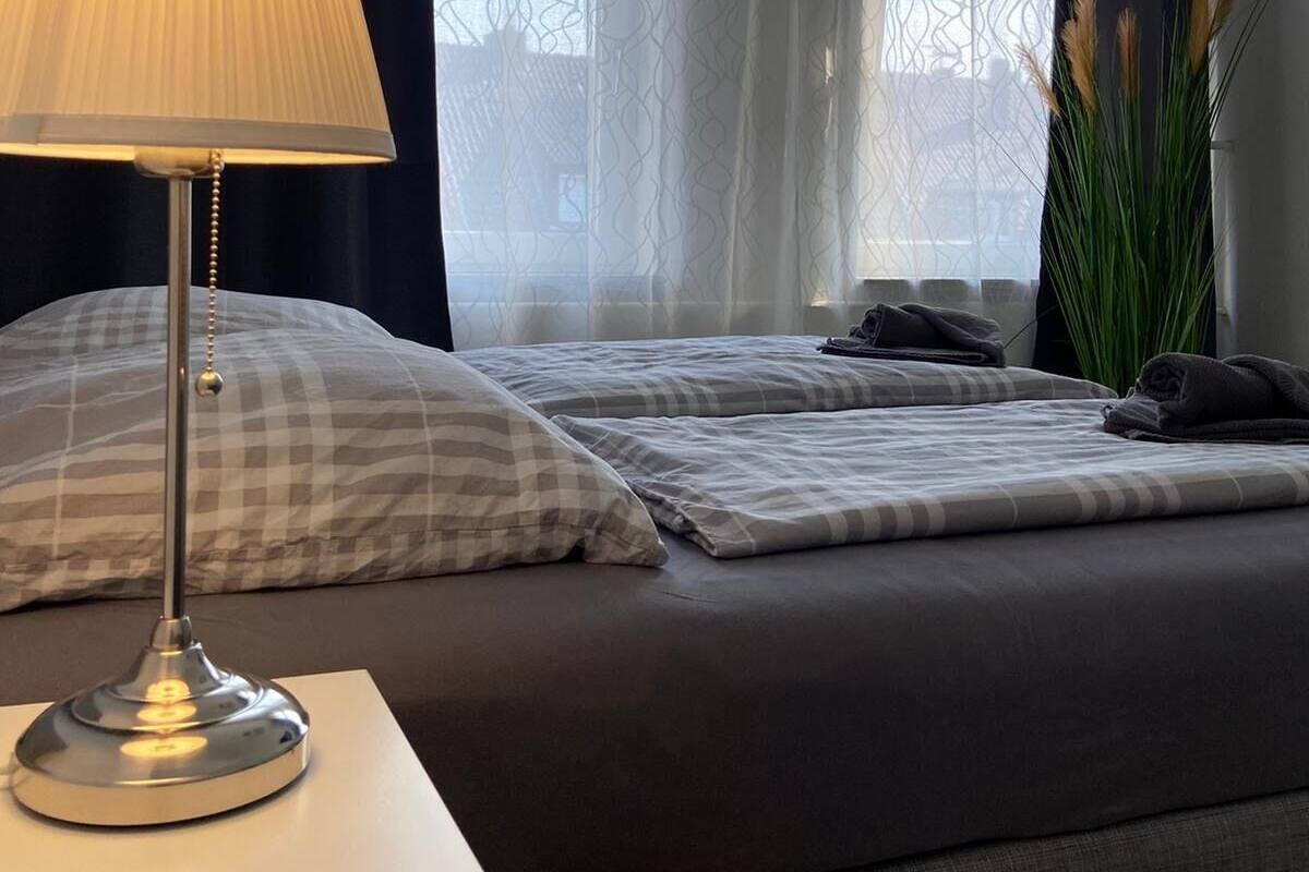 A bedroom with two beds, a bedside table with a lamp, and a window with sheer curtains.