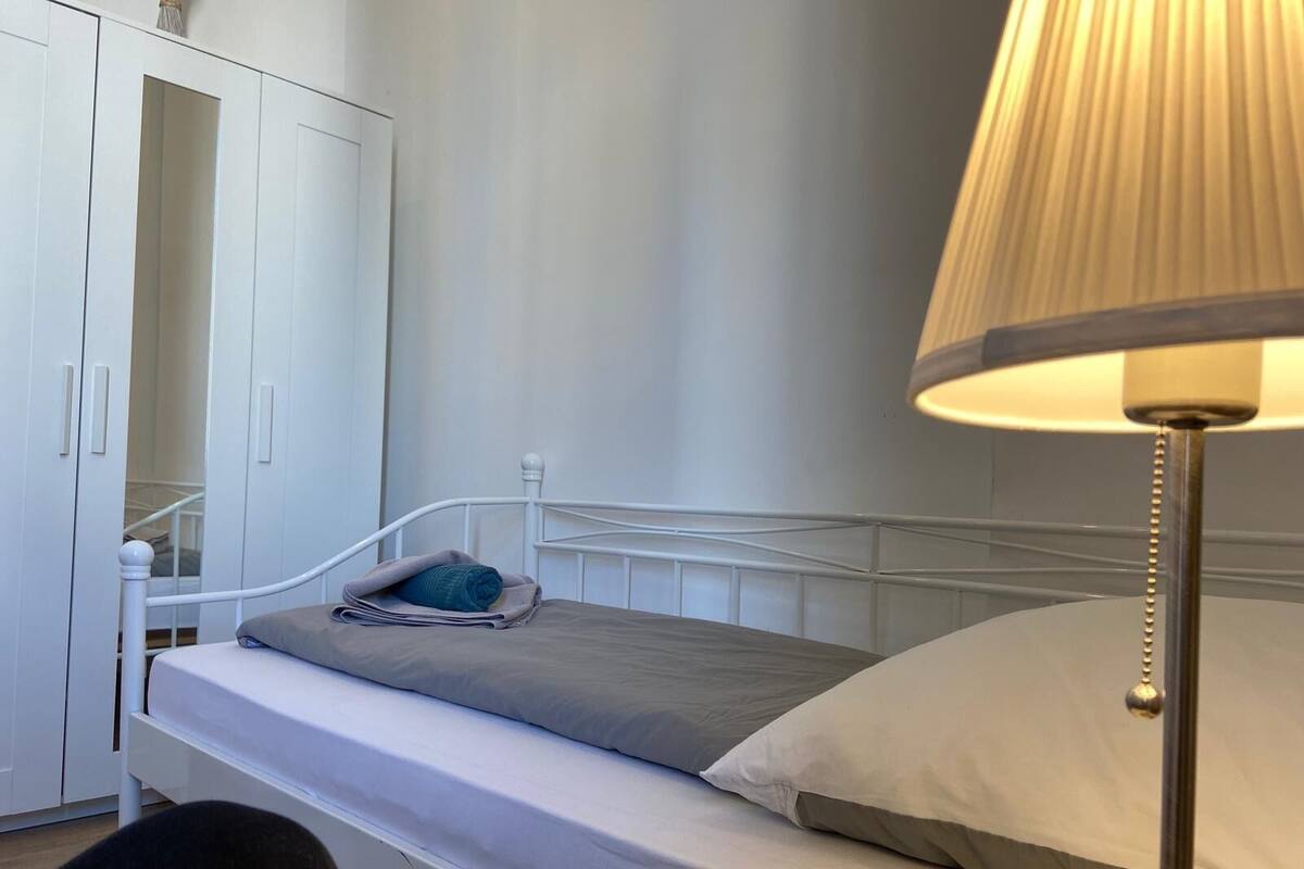 A single bed with a grey mattress, a white headboard, and a bedside lamp.