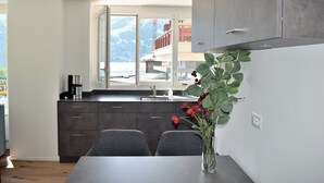 A modern kitchen with dark cabinets, a large window, and a dining area with a table and chairs. - Apartement Eigerpeak (Lauterbrunnen)