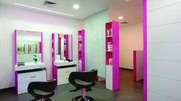 Un moderno salón con dos sillas de peluquería negras, estanterías blanco y rosa, y un diseño limpio y contemporáneo.
