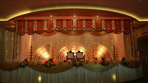 Un escenario con un telón de fondo semicircular, cortinas decorativas y arreglos florales.