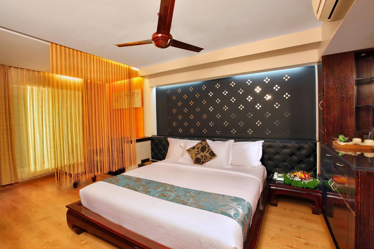 Habitación de hotel con cama, ventilador de techo, mesita de noche con lámpara y aire acondicionado instalado en la pared.