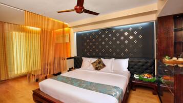 A hotel room with a bed, a ceiling fan, a nightstand with a lamp, and a wall-mounted air conditioner.