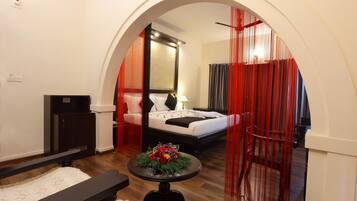 A hotel room with a bed, a bedside table with a floral arrangement, a desk, and a wardrobe.