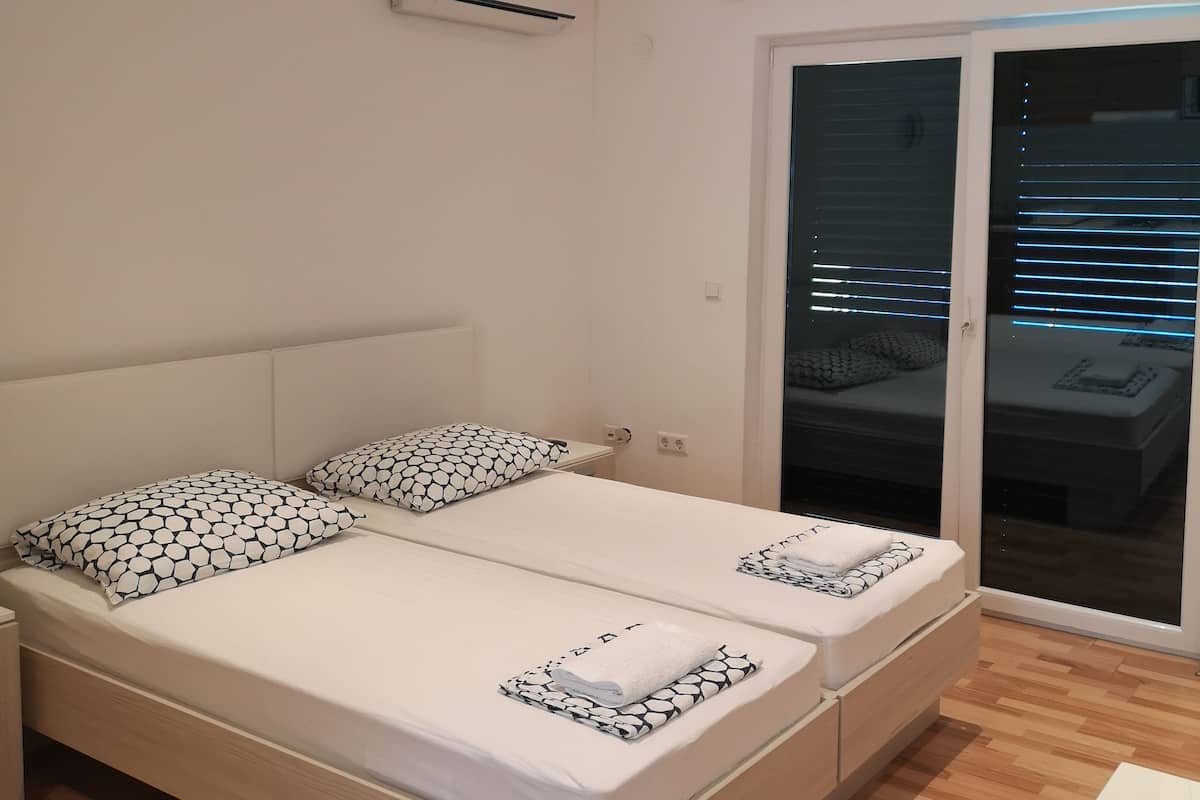 A modern bedroom with a large bed, two bedside tables, a built-in air conditioning unit, and a sliding glass door leading to a balcony.